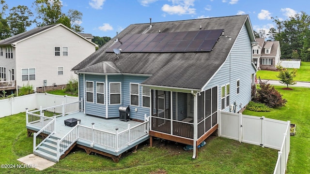 rear view of house with a sunroom, solar panels, a deck, and a yard