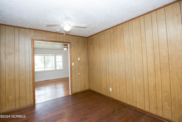 unfurnished room with a textured ceiling, dark hardwood / wood-style flooring, wood walls, ceiling fan, and ornamental molding