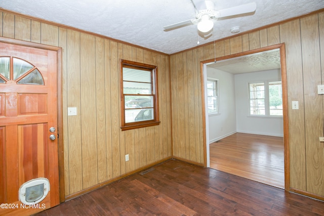 entryway featuring dark hardwood / wood-style flooring, wooden walls, ceiling fan, and a textured ceiling