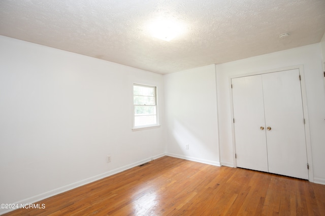 unfurnished bedroom featuring a textured ceiling, hardwood / wood-style floors, and a closet