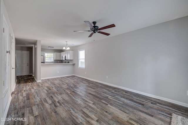 unfurnished living room with ceiling fan with notable chandelier and dark hardwood / wood-style flooring