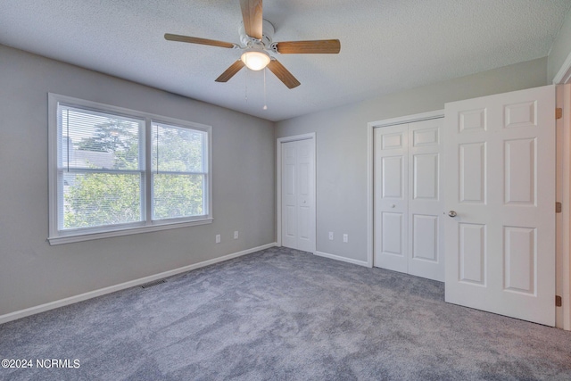 unfurnished bedroom with a textured ceiling, ceiling fan, carpet floors, and two closets