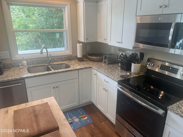 kitchen with dark wood-type flooring, white cabinets, light stone countertops, stainless steel appliances, and sink