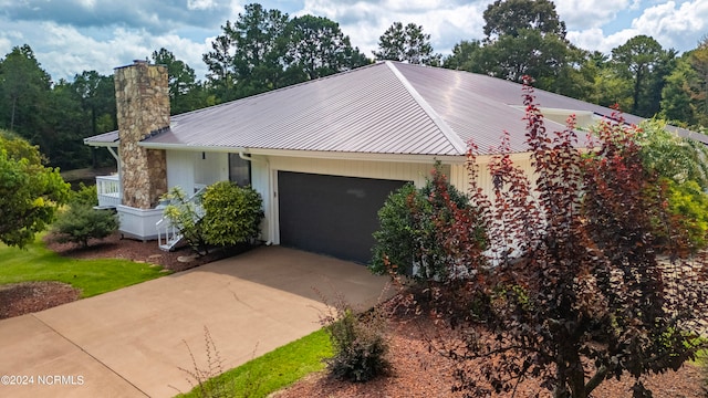 ranch-style house featuring a garage, a chimney, metal roof, and concrete driveway