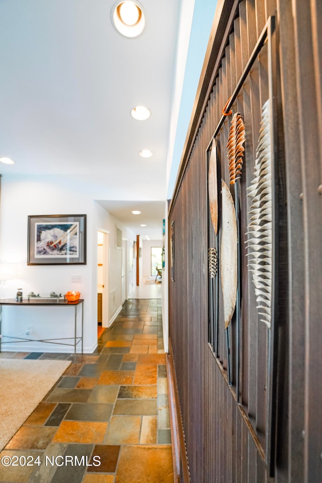 corridor featuring baseboards, stone tile flooring, and recessed lighting