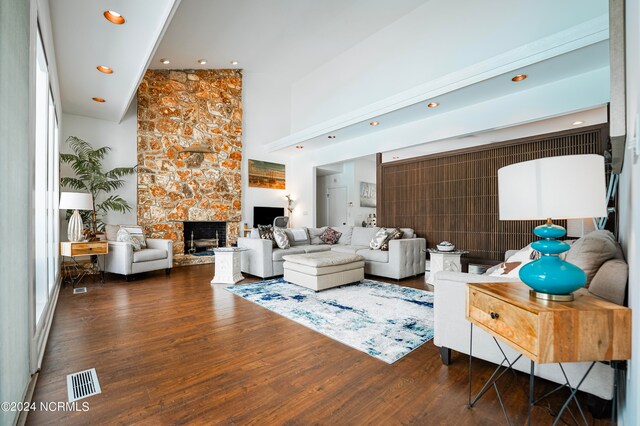 living room featuring recessed lighting, visible vents, a high ceiling, a stone fireplace, and wood finished floors