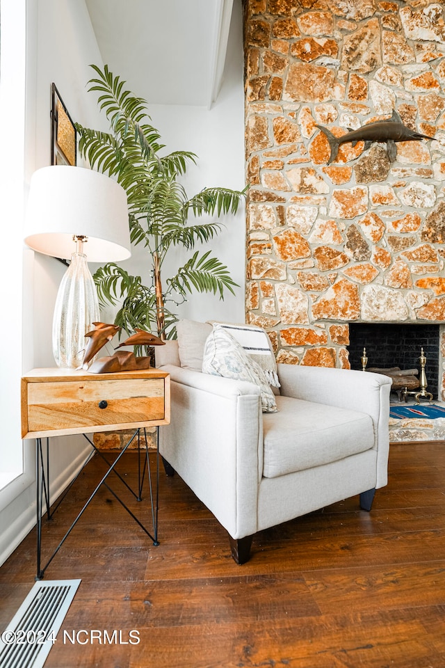 sitting room with a stone fireplace and dark wood-type flooring