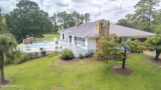 back of property with metal roof, central air condition unit, fence, a lawn, and a chimney