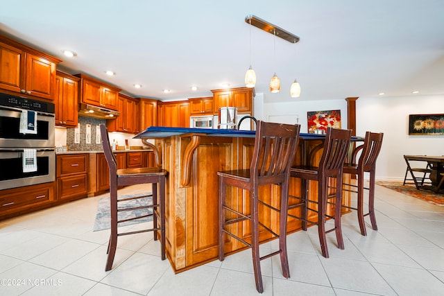 kitchen featuring under cabinet range hood, light tile patterned floors, appliances with stainless steel finishes, and a breakfast bar