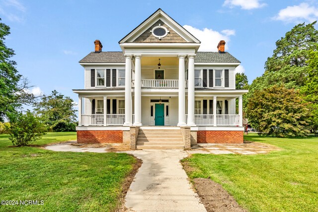 greek revival inspired property featuring a shingled roof, a balcony, a chimney, covered porch, and a front lawn