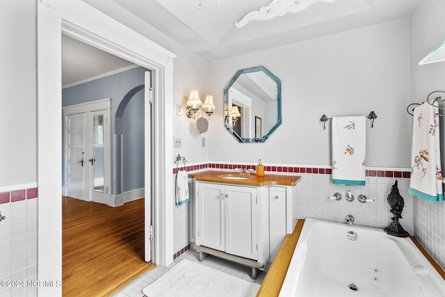 full bath featuring a wainscoted wall, wood finished floors, vanity, tile walls, and a whirlpool tub