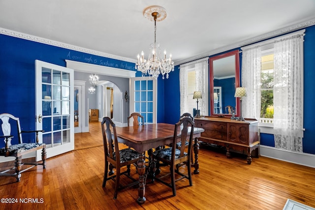 dining space featuring wood-type flooring, arched walkways, a chandelier, and baseboards