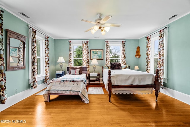 bedroom with baseboards, wood finished floors, visible vents, and crown molding