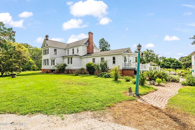 rear view of property featuring a deck, a lawn, and a chimney