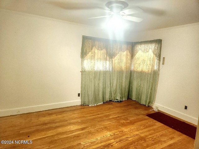 empty room featuring ornamental molding, wood finished floors, a ceiling fan, and baseboards