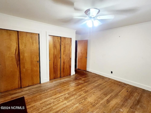 unfurnished bedroom with crown molding, two closets, a ceiling fan, wood finished floors, and baseboards