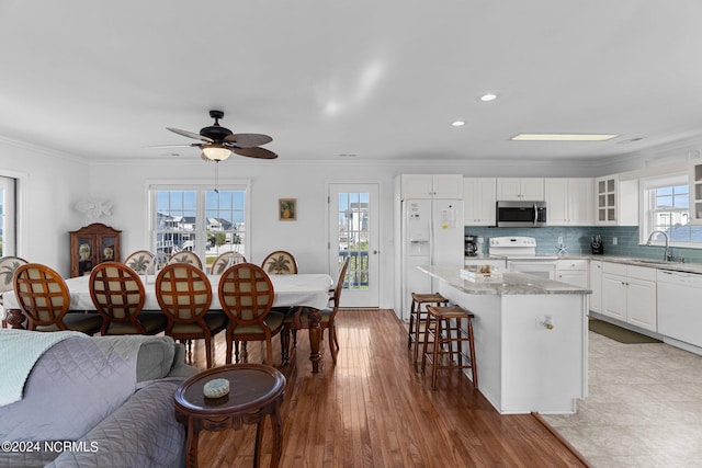 kitchen with a center island, crown molding, a sink, white appliances, and a kitchen bar