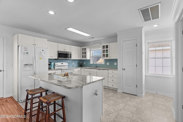 kitchen featuring white appliances, a breakfast bar, visible vents, ornamental molding, and glass insert cabinets