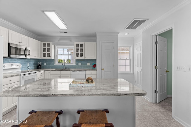 kitchen with white appliances, a breakfast bar, a sink, visible vents, and crown molding