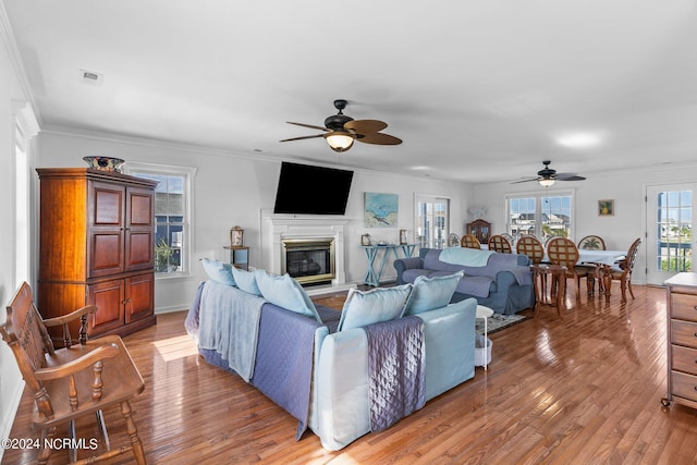 living area with a glass covered fireplace, visible vents, crown molding, and light wood-style flooring