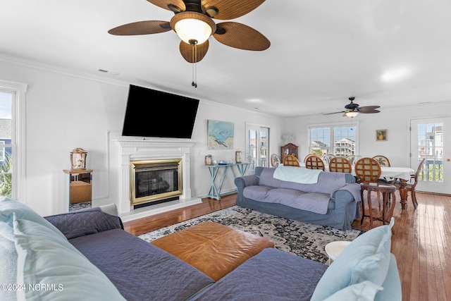 living area with visible vents, ornamental molding, wood finished floors, and a glass covered fireplace