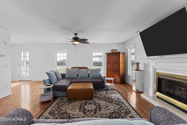 living area featuring a fireplace with raised hearth, wood finished floors, a ceiling fan, baseboards, and ornamental molding