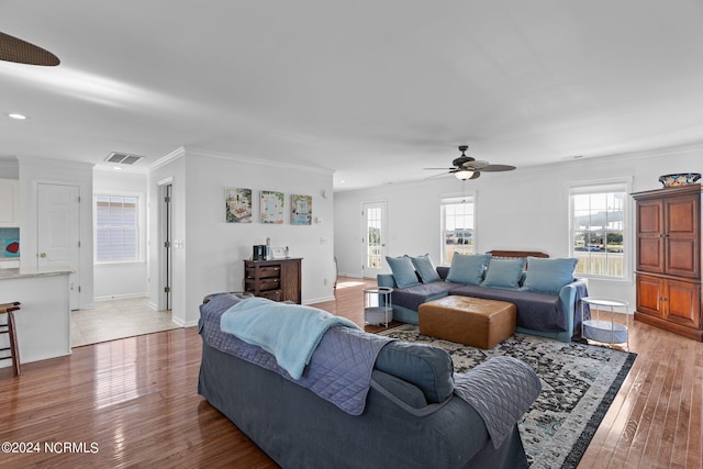 living room with crown molding, light wood-style flooring, visible vents, and a healthy amount of sunlight