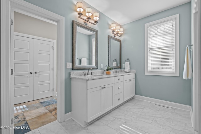 bathroom featuring marble finish floor, a sink, baseboards, and double vanity