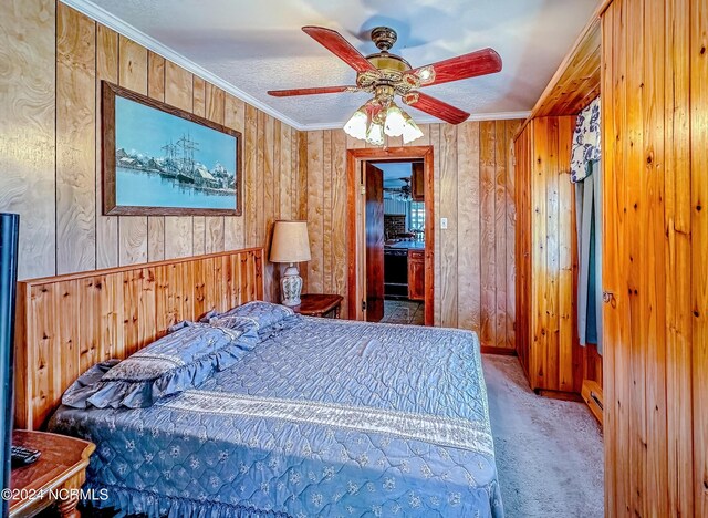 carpeted bedroom with a baseboard radiator, ceiling fan, a textured ceiling, crown molding, and wood walls