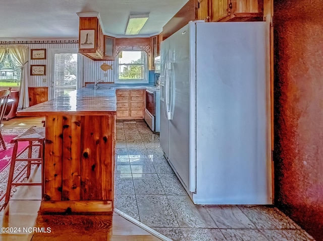 kitchen with a peninsula, white refrigerator with ice dispenser, range with electric stovetop, a breakfast bar, and a sink