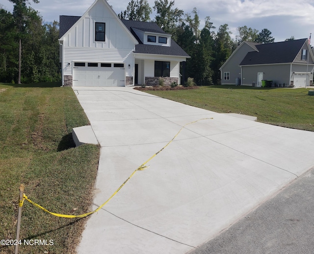 modern farmhouse style home with an attached garage, stone siding, driveway, board and batten siding, and a front yard