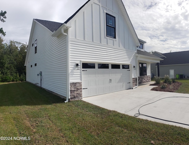 view of side of home featuring driveway, a lawn, stone siding, an attached garage, and board and batten siding