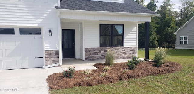 entrance to property featuring covered porch, stone siding, a yard, and roof with shingles