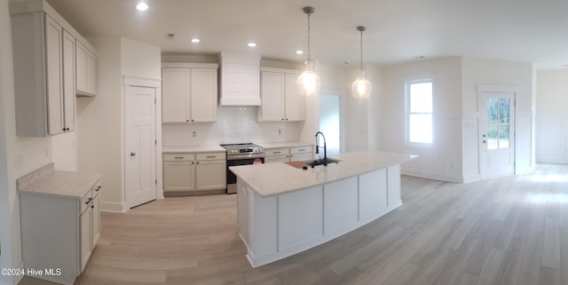 kitchen with a sink, light wood-type flooring, stainless steel range with electric stovetop, premium range hood, and backsplash