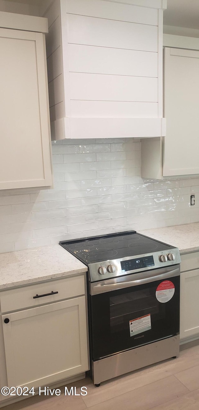 kitchen featuring tasteful backsplash, white cabinets, light wood-style flooring, light stone countertops, and stainless steel electric range