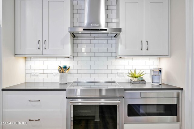 kitchen with dark countertops, stainless steel electric range oven, decorative backsplash, white cabinetry, and wall chimney exhaust hood