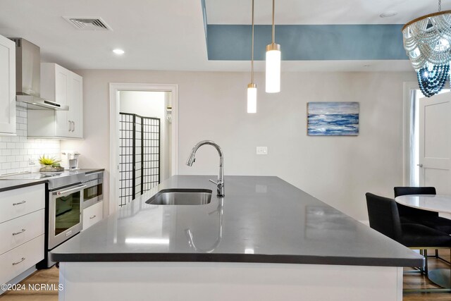 kitchen featuring visible vents, stainless steel range with electric stovetop, a sink, dark countertops, and wall chimney range hood