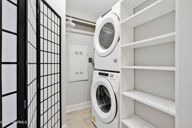 clothes washing area featuring tile patterned flooring, laundry area, stacked washer and clothes dryer, and baseboards