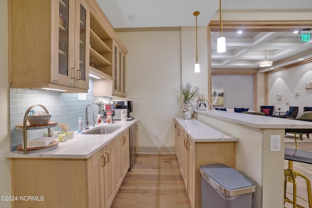 kitchen featuring coffered ceiling, a peninsula, light wood-style flooring, a sink, and decorative backsplash