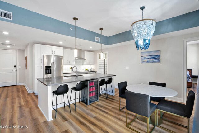 kitchen with a breakfast bar area, beverage cooler, visible vents, stainless steel fridge with ice dispenser, and wall chimney exhaust hood