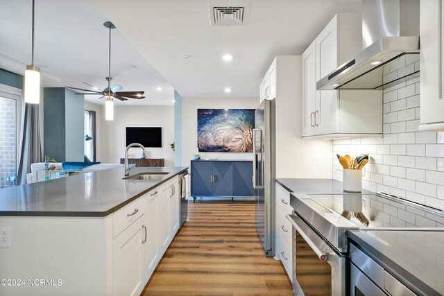 kitchen featuring visible vents, a sink, dark countertops, stainless steel appliances, and wall chimney exhaust hood