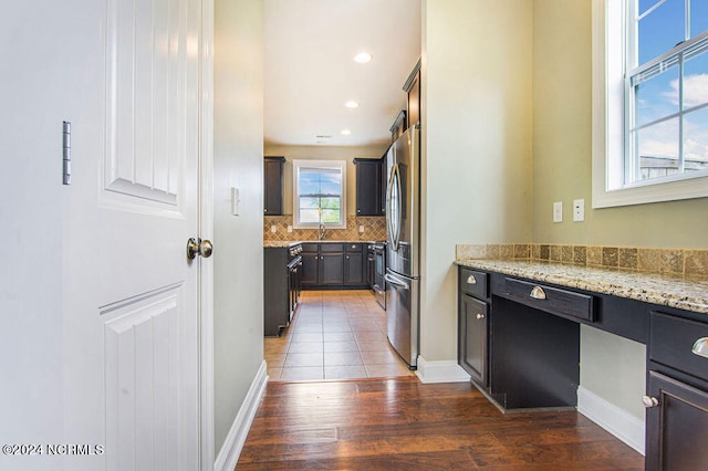 kitchen featuring stainless steel fridge, decorative backsplash, dark hardwood / wood-style floors, and light stone counters