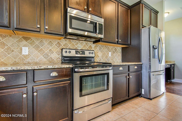 kitchen featuring light tile patterned flooring, stainless steel appliances, dark brown cabinetry, light stone counters, and decorative backsplash