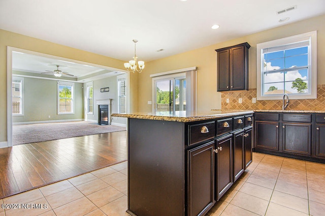 kitchen with decorative backsplash, light hardwood / wood-style flooring, hanging light fixtures, a center island, and ceiling fan with notable chandelier