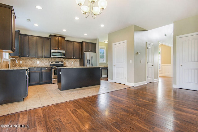 kitchen featuring stainless steel appliances, a center island, a notable chandelier, light wood-type flooring, and light stone counters