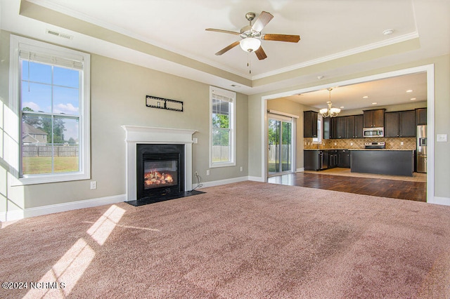 unfurnished living room featuring ornamental molding, ceiling fan with notable chandelier, dark carpet, and a raised ceiling