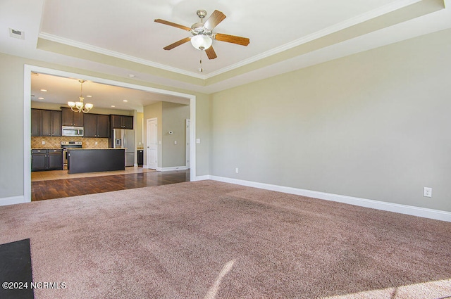 unfurnished living room featuring crown molding, ceiling fan with notable chandelier, dark carpet, and a raised ceiling