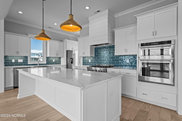 kitchen featuring appliances with stainless steel finishes, light hardwood / wood-style floors, crown molding, a center island, and hanging light fixtures