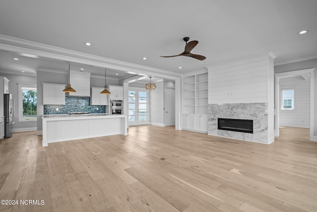 unfurnished living room with a fireplace, light hardwood / wood-style flooring, built in shelves, ornamental molding, and ceiling fan