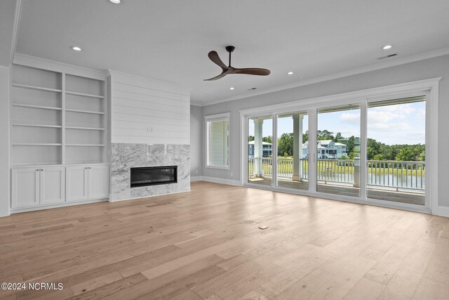 unfurnished living room with a high end fireplace, crown molding, ceiling fan, and light hardwood / wood-style floors